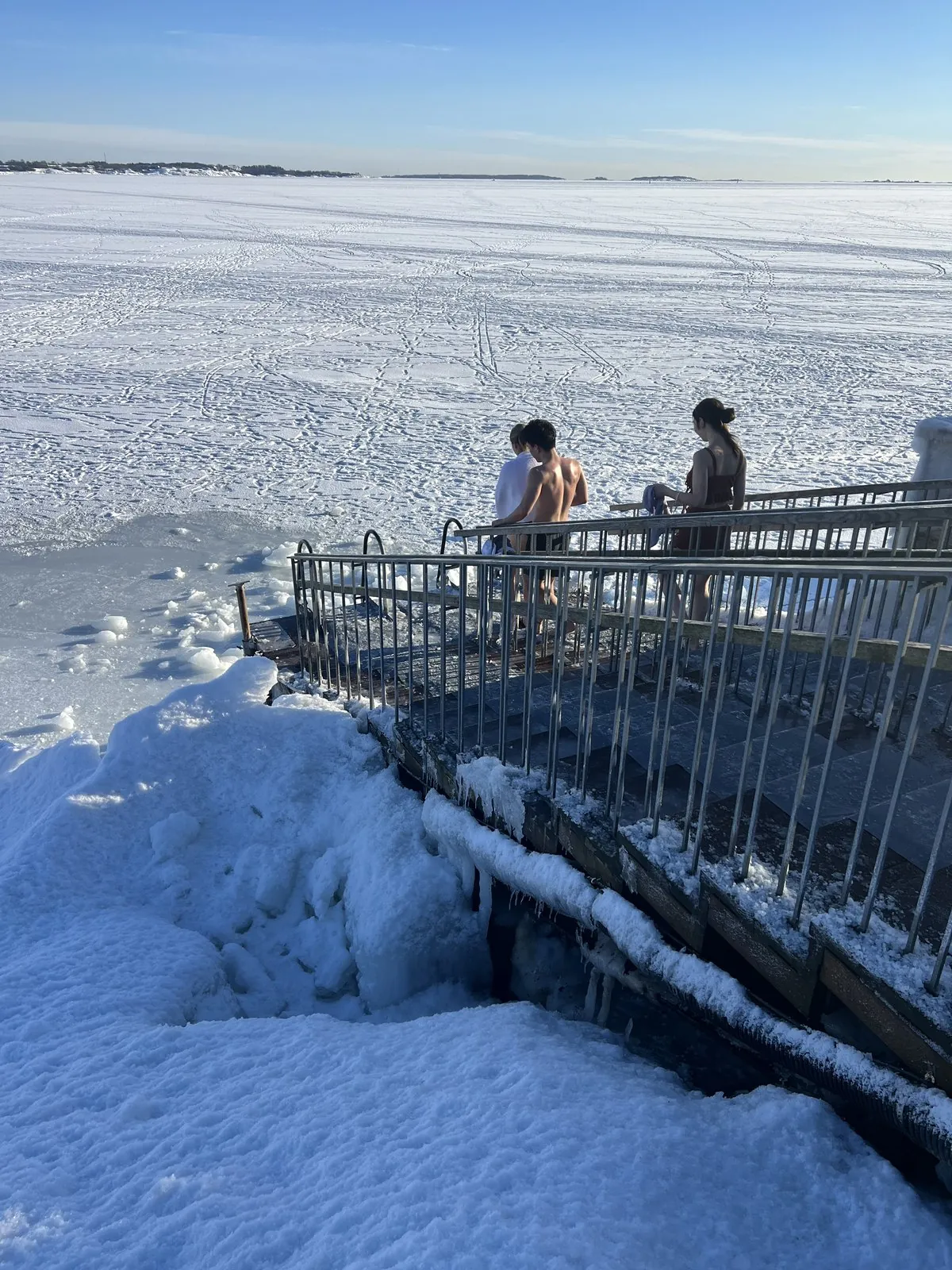 氷結した海の氷穴デッキで涼む水着姿の人たち
