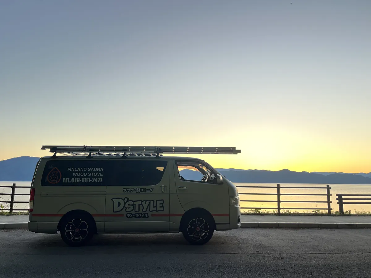 湖のほとりの道に停めたD'STYLEの作業車。屋根にはしごを積み、うしろに夕焼けの湖と山なみ