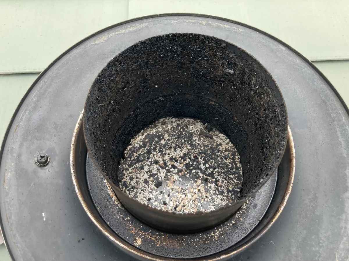 上からのぞいた煙突の筒。内側に黒いススが付き、底に白っぽい燃えかすが積もっている