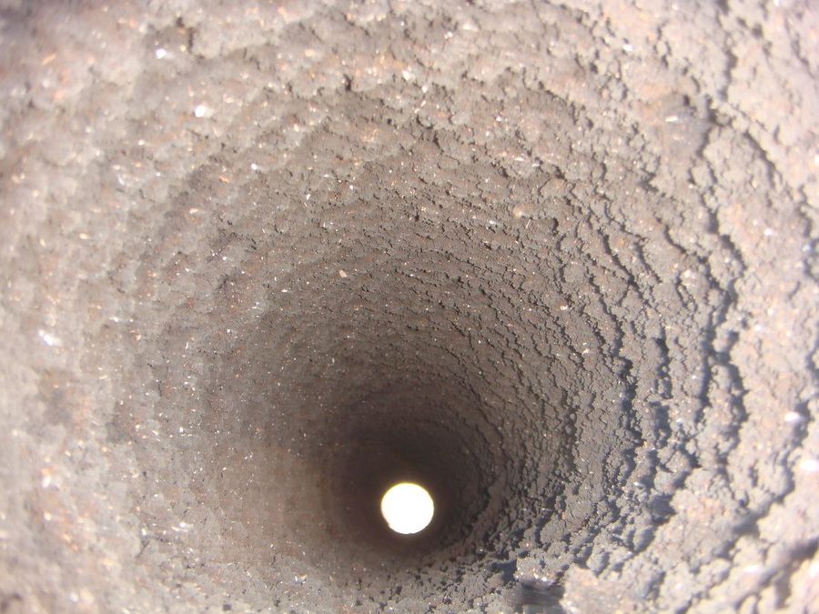 煙突の中を筒の方向にのぞいた写真。内壁一面がザラザラしたススの層で厚く覆われ、奥の出口が小さな光の点になっている