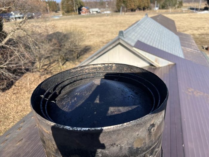 掃除を終えた煙突トップを屋根の上から見下ろした写真。内側のタールは落ち、なめらかな金属の面が見えている