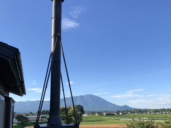 支線で支えた黒い煙突と、青空、田んぼ、遠くの山