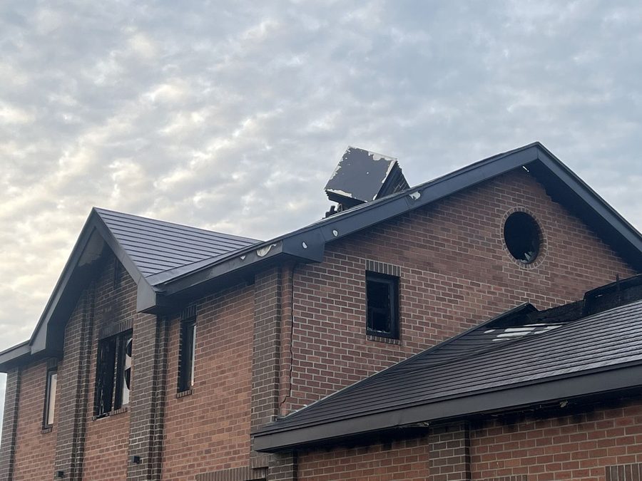 火災に遭ったレンガ造りの住宅の屋根。角型の煙突トップがあった場所は、ねじれた金属を残して失われている。窓は黒い開口部になっている