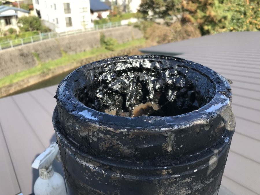 屋根の上の煙突の口を見下ろした写真。黒く濡れたように光るタールが厚く固まり、煙の通り道がほとんど塞がっている