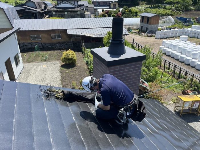 屋根の上で、ヘルメットと安全帯を着けてブラシで煙突を掃除する職人