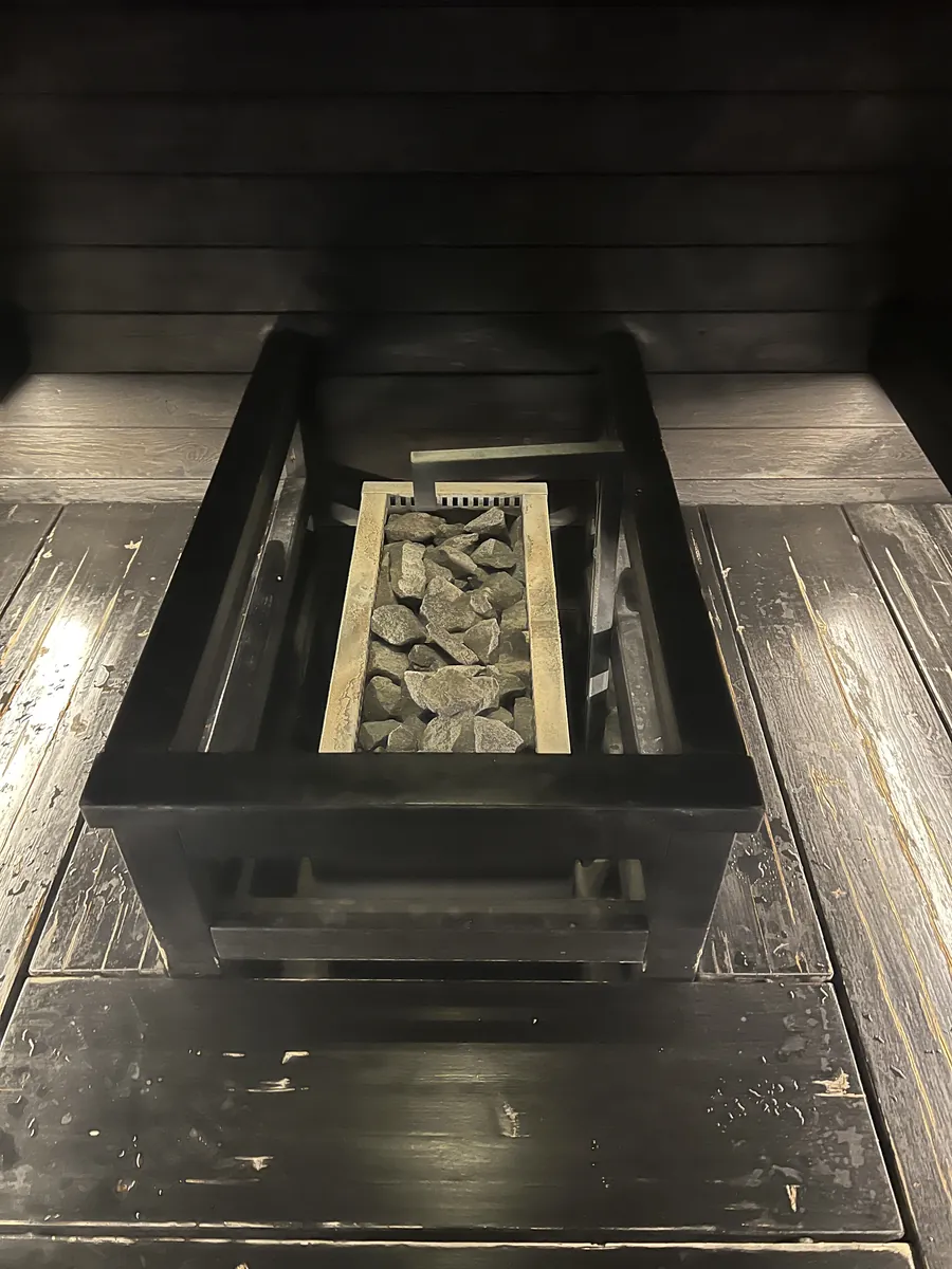 黒く焼いた板壁に埋め込まれた黒い鉄の炉。金網の奥にサウナストーンが詰まっている