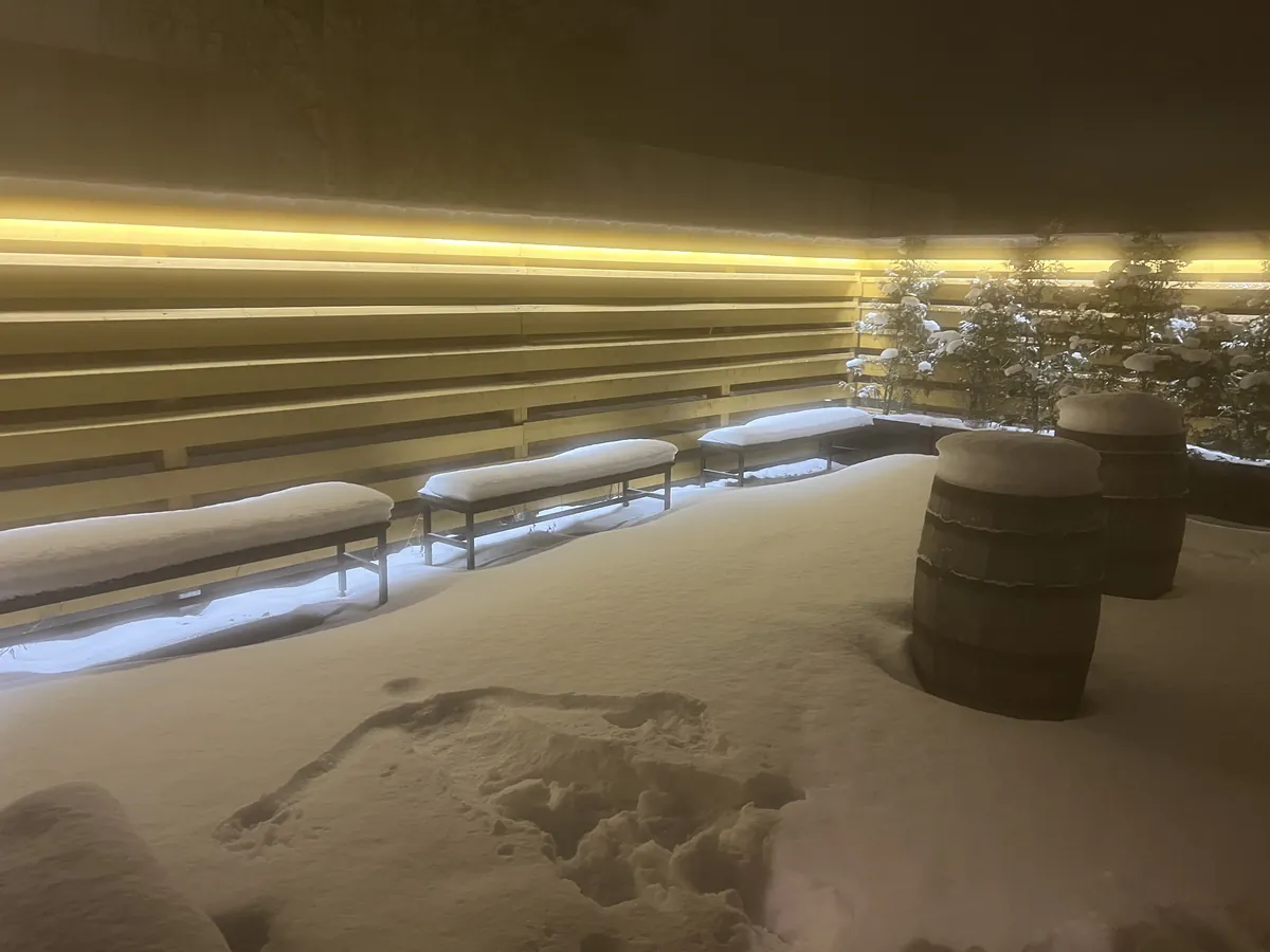 ユヴァスキュラのサウナ施設の雪のテラス。間接照明に照らされた木の壁と、雪をかぶったベンチが並ぶ
