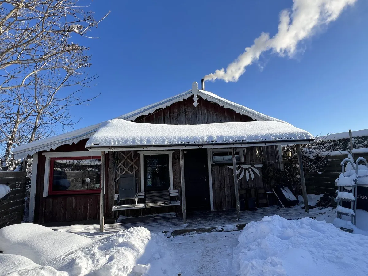 雪をかぶった伝統的な木造サウナ小屋と、煙突から立ちのぼる煙