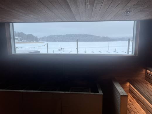 凍った湖を望むサウナ室の窓と、外の雪原を歩く人影