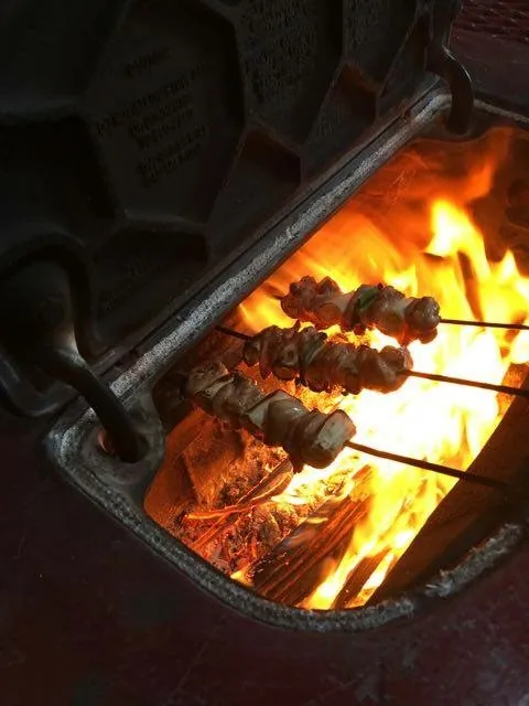 薪ストーブの炎の上で焼く、肉の串。