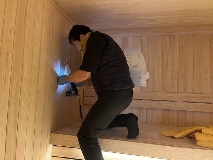 サウナ室の壁に飾りを取り付ける職人。白木の室内での造作作業
