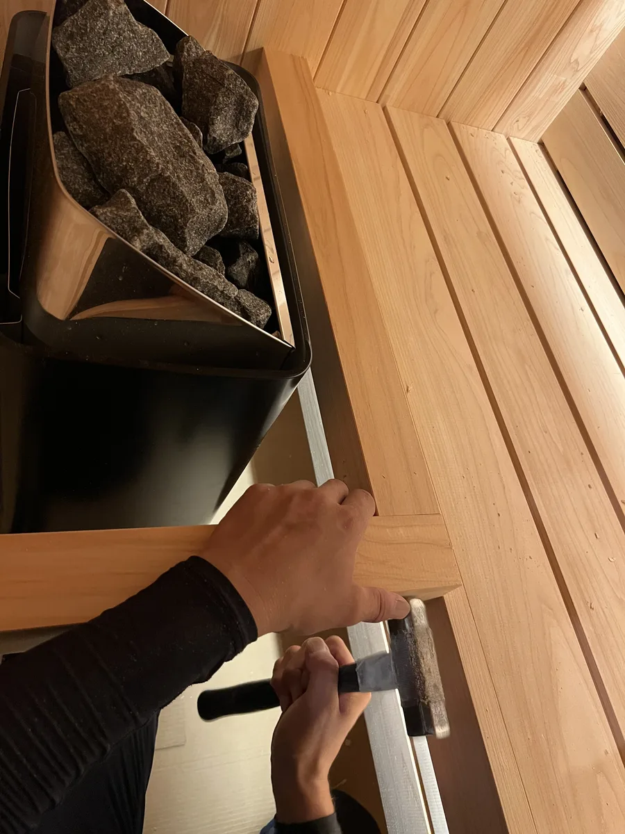 ハルビアのヒーターの脇に、ベンチ材を納める職人の手