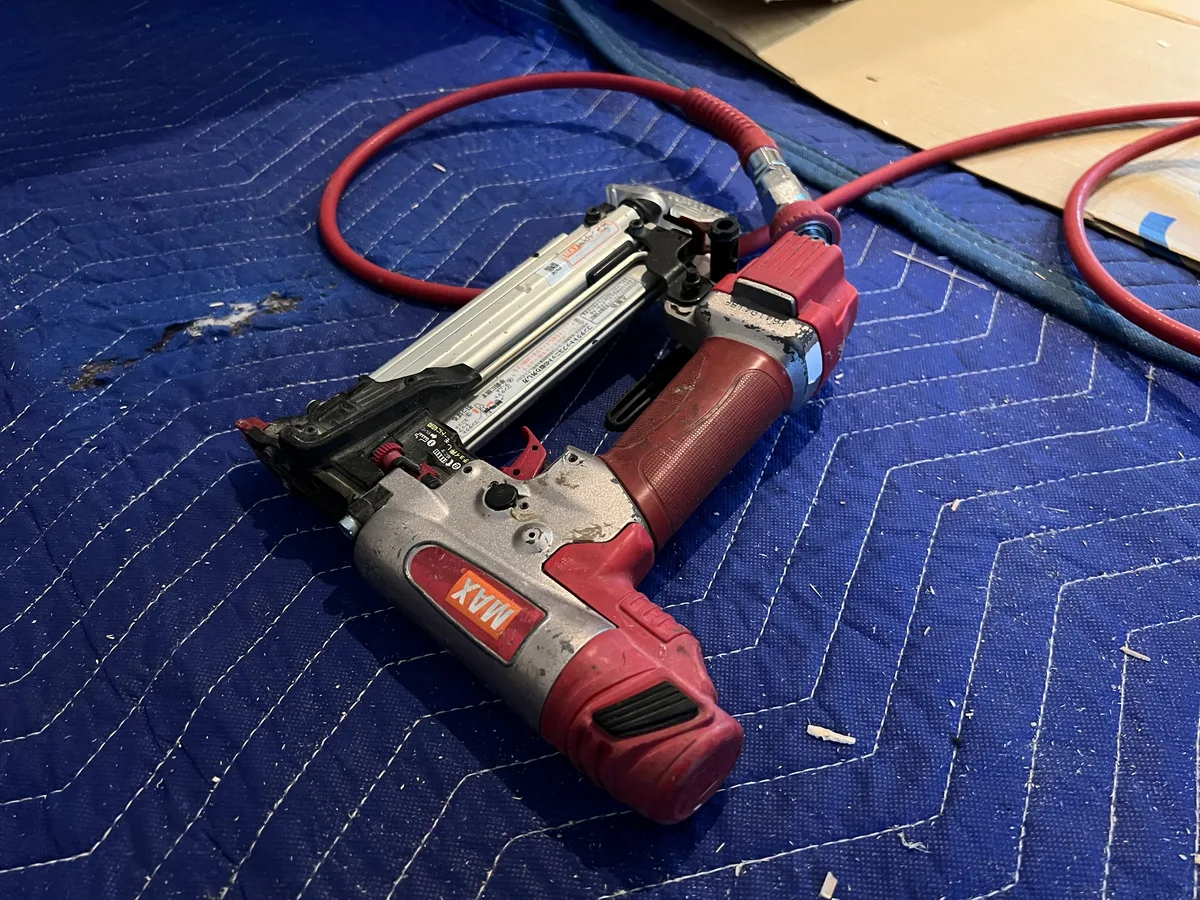 毛布の上に置かれた仕上げ用の釘打機とエアホース