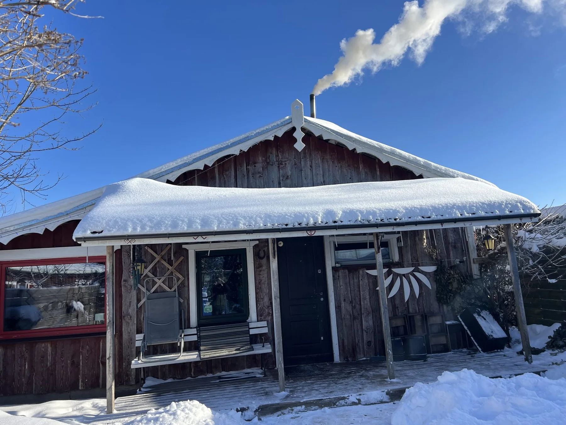 雪に囲まれた木造小屋と、煙突から立ちのぼる煙、冬の青空