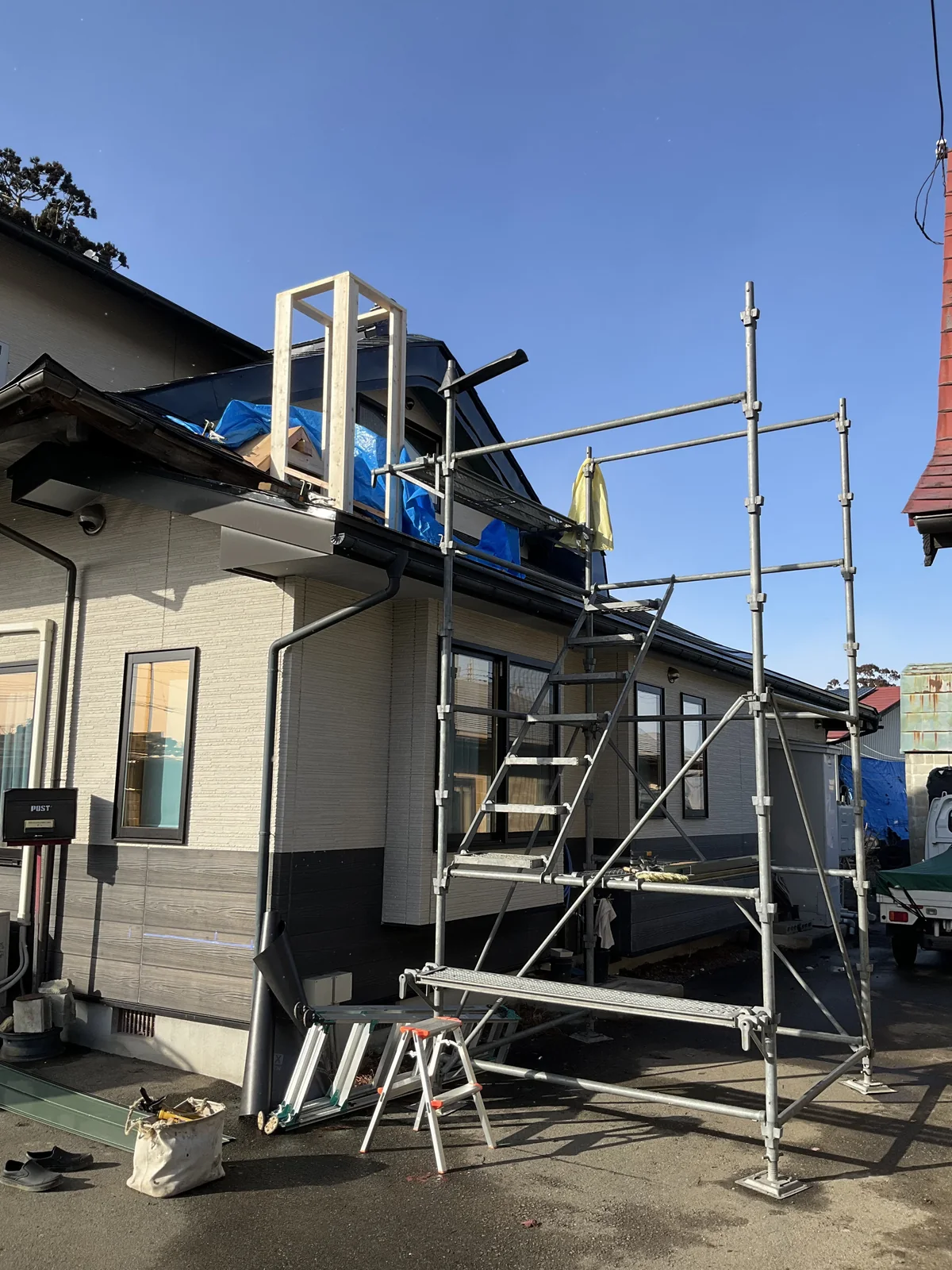 足場を組んだ平屋。屋根の上にブルーシートが掛かり、その中から新しい木枠が立ち上がっている