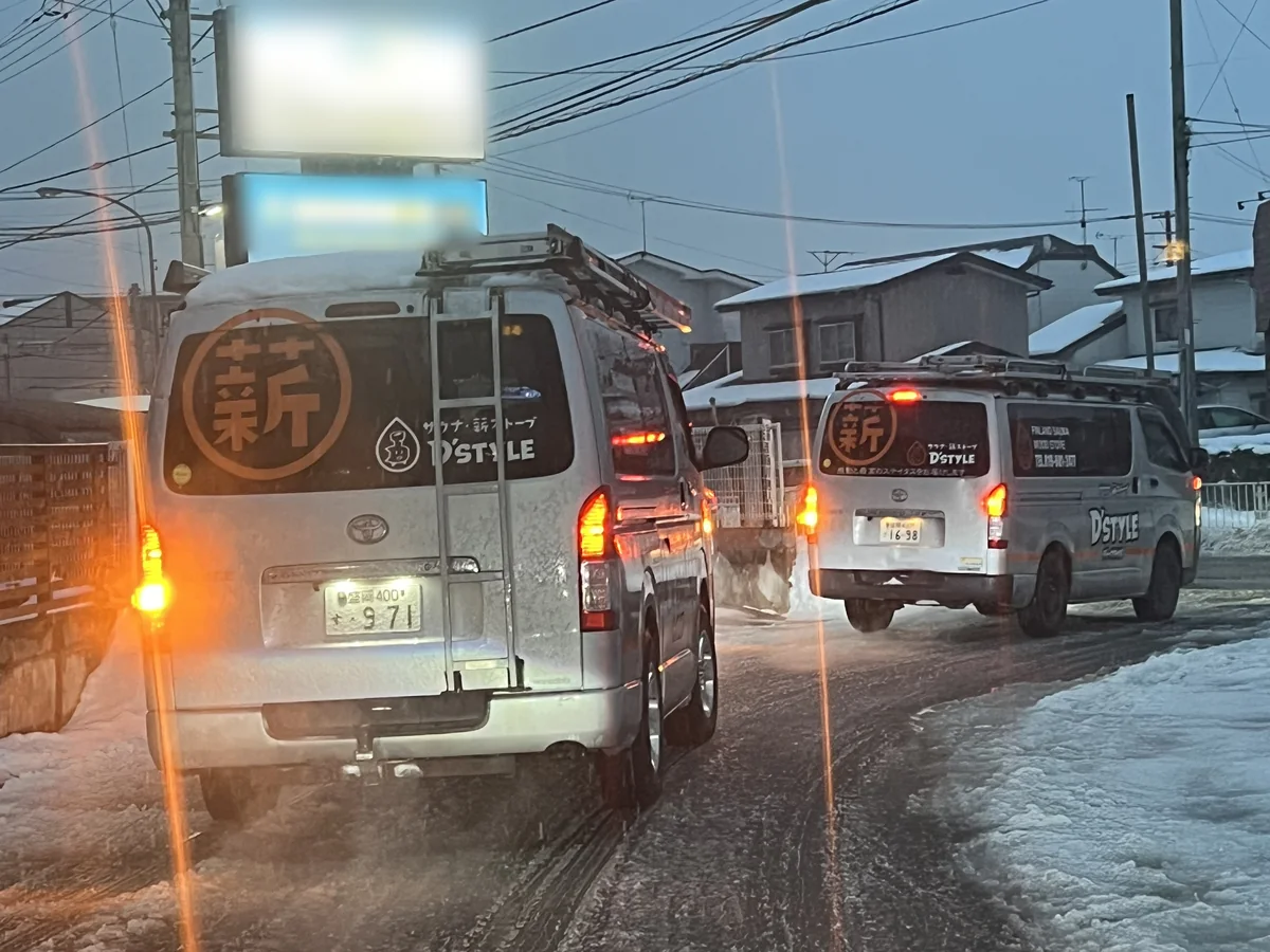 雪の降る道に停まる2台の作業車。ハザードランプがついている