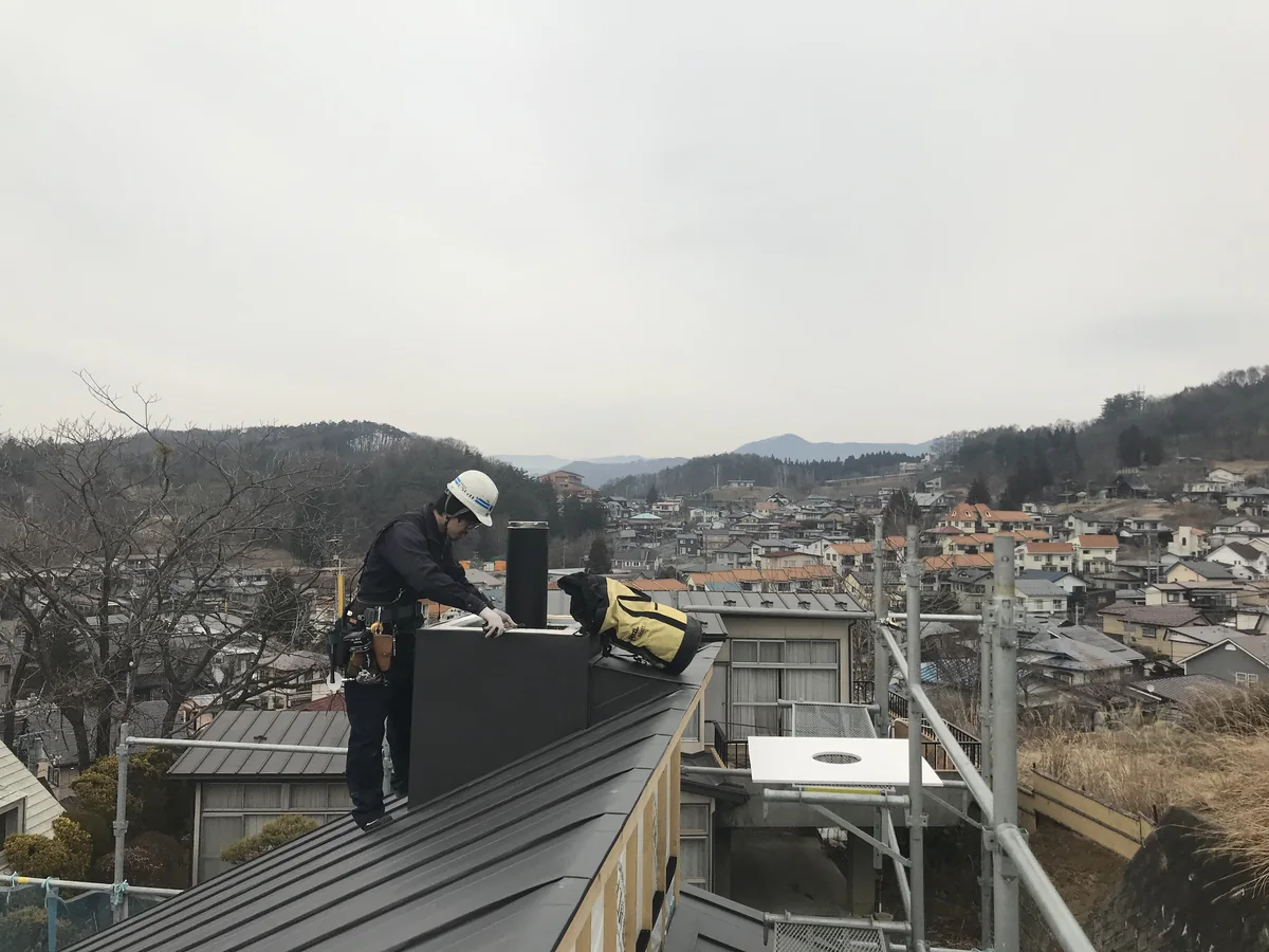 町を見下ろす屋根の上で、煙突の囲いを組み立てているところ