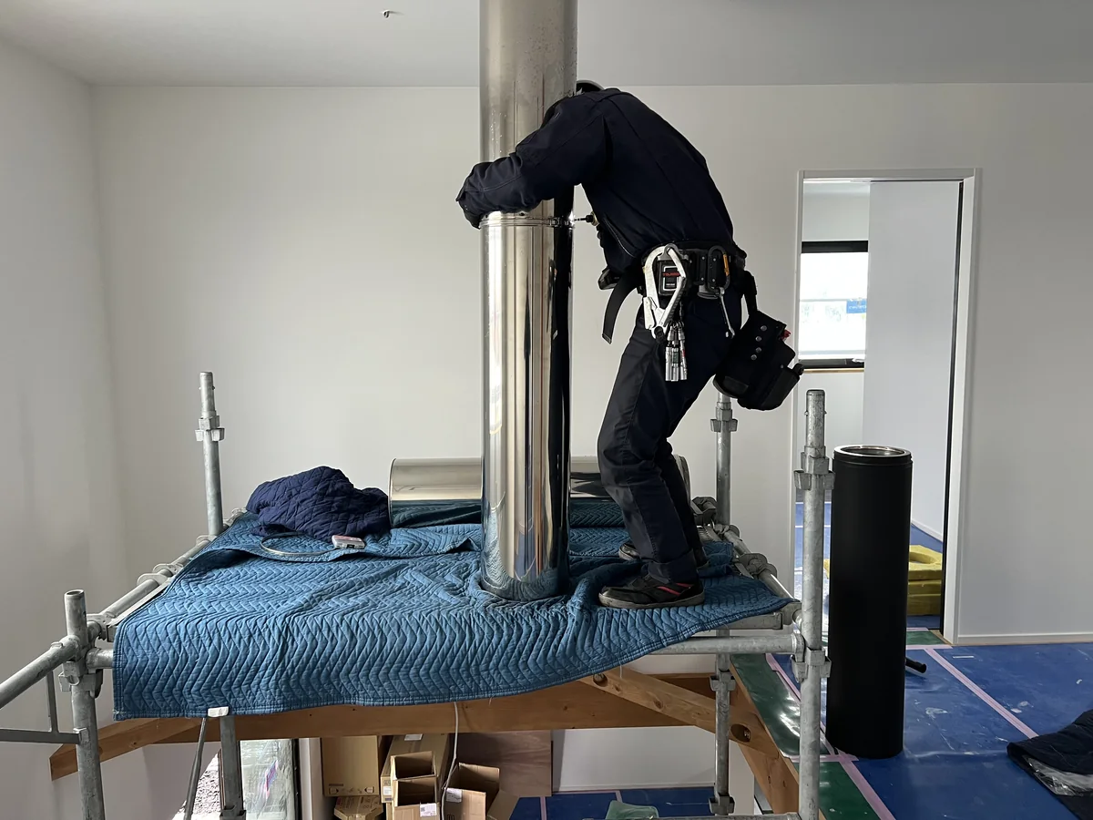 室内に組んだ足場の上で、天井へ抜ける煙突の継ぎ目を締めているところ