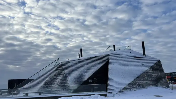 ヘルシンキ南端の海沿いに建つ公共サウナ。木のルーバーが斜めに立ち上がり、雪をかぶった屋根の上に人が歩ける階段がついている