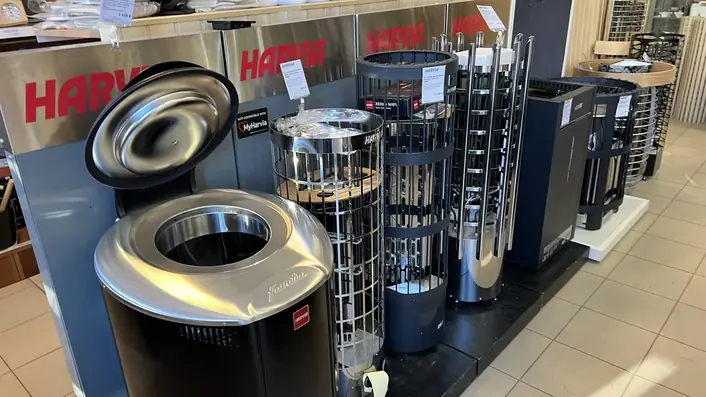 リトアニアのサウナ資材店の売り場。赤いHARVIAの看板の下に、電気サウナヒーターが数台並べて展示されている