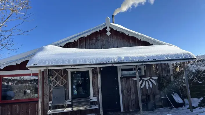 雪に覆われた木造小屋の煙突から煙が立ちのぼる冬の風景