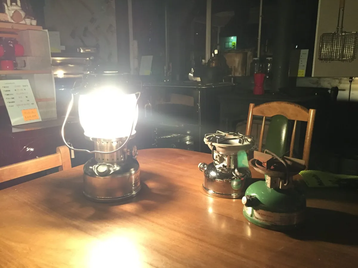 夜の工房。直したコールマンのランタンが灯り、隣にレストアを終えたストーブが並ぶ