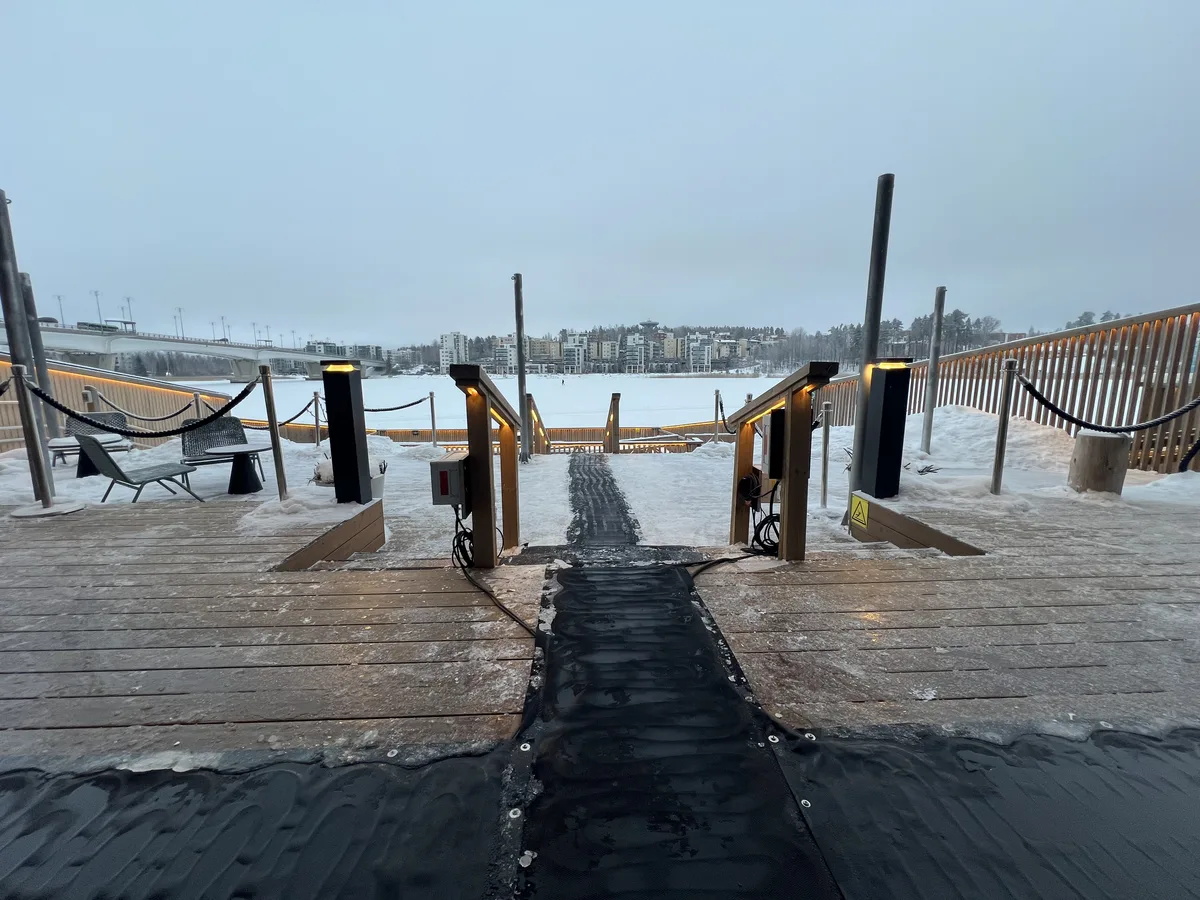 フィンランドのサウナ施設から凍った湖へ続く桟橋。温かい照明と雪景色