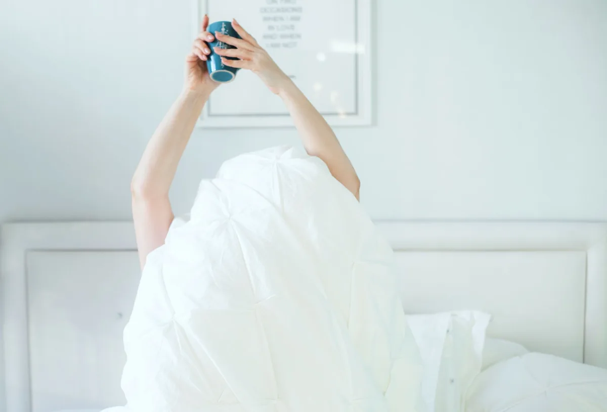 白いシーツの上でコーヒーを飲む人