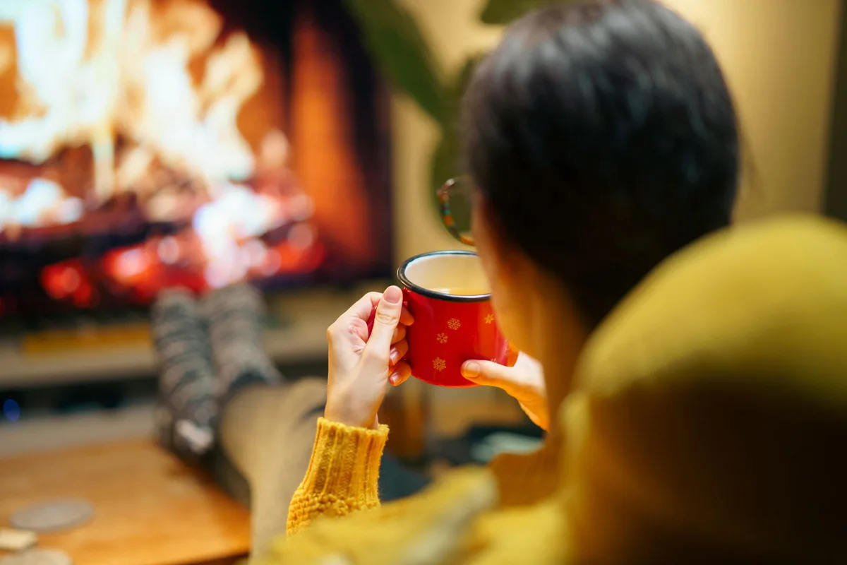 冬の夕方に暖炉のそばで温かい飲み物を楽しむ女性