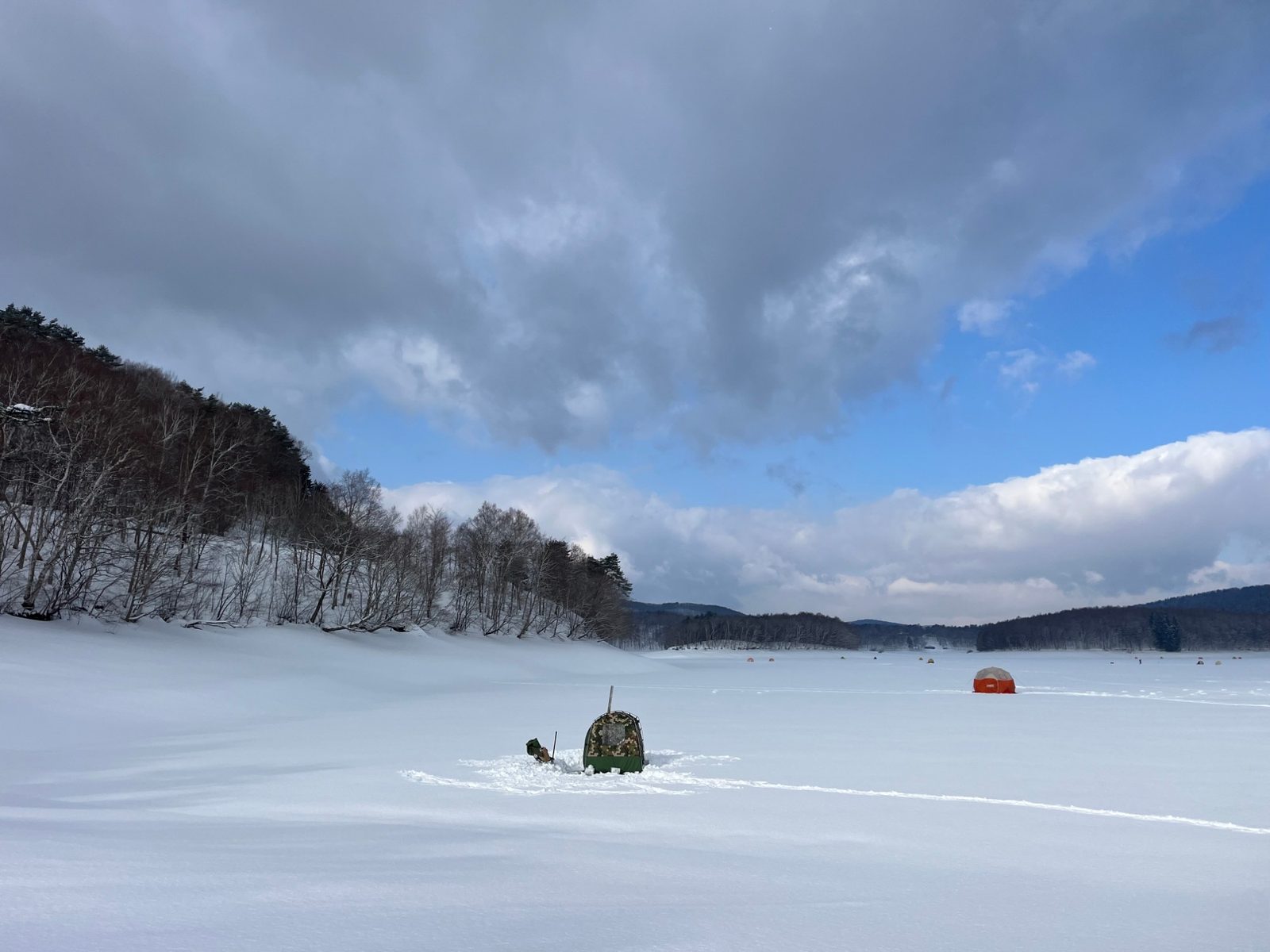 凍結した湖の雪原に点在するテント。遠くまで見渡せる冬の景色